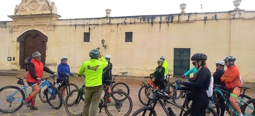 A group of cyclists gathered around a building with a large door and decorative elements. 4
