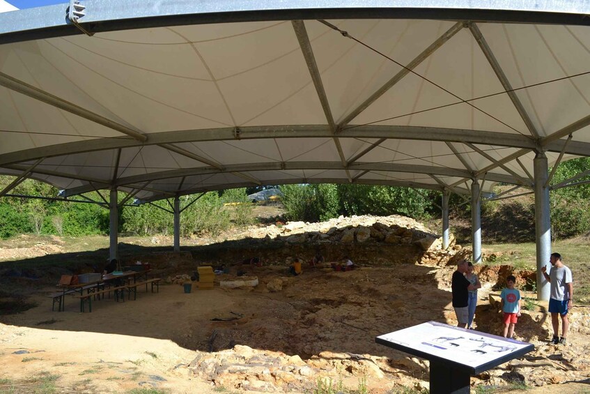 An archaeological site with a covered area, tables, and people observing. 2