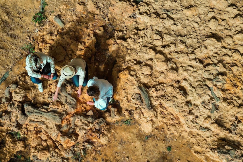 Three people excavating a large, dry, rocky pit. 1