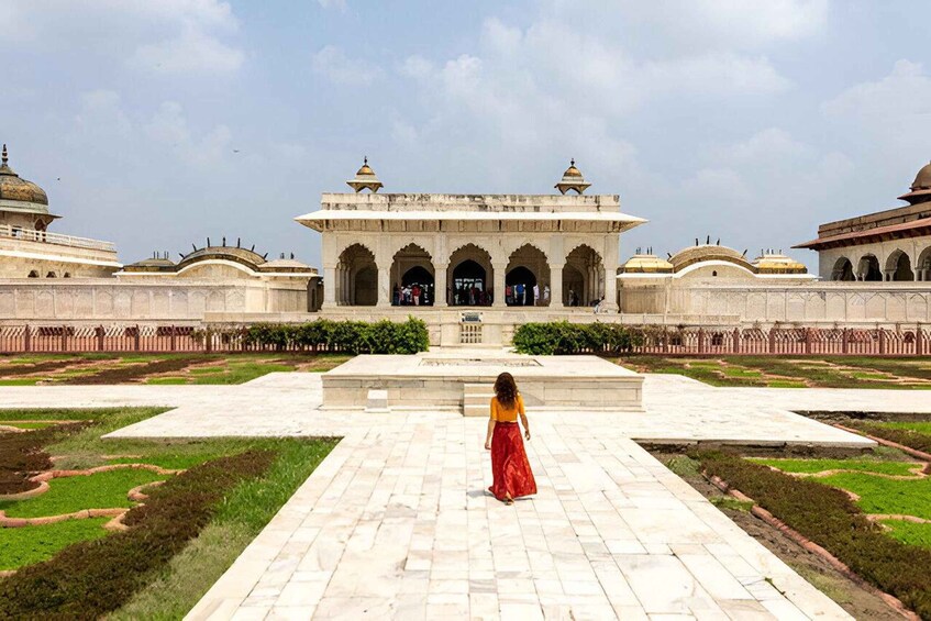 A historical building with arches and domes, a central courtyard, and a person walking towards it. 3
