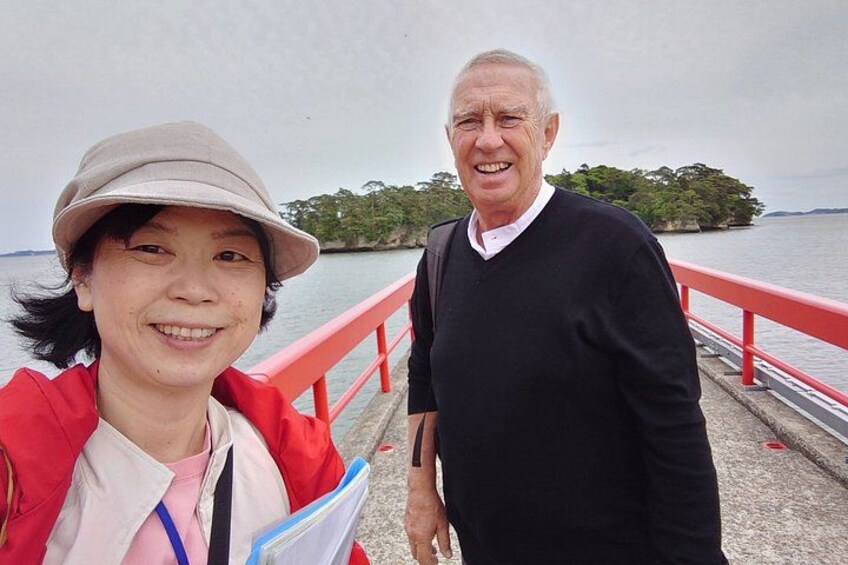 Two people standing on a bridge with a body of water and a landmass in the background. 4