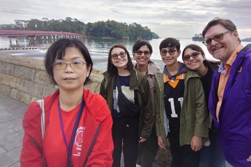 A group of people standing by a waterfront with a bridge in the background. 1
