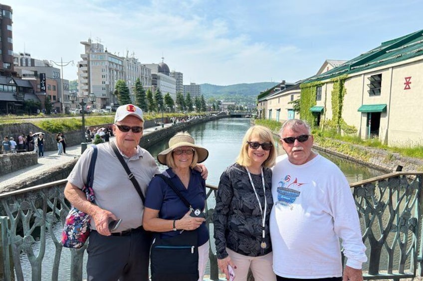 A group of people standing on a bridge with a river and buildings in the background. 1