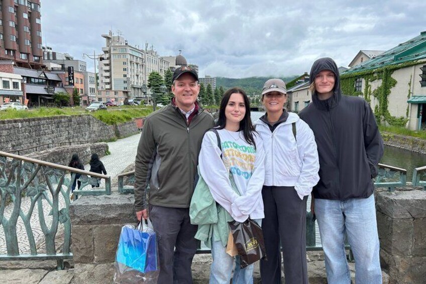 A group of people standing on a bridge with a river and buildings in the background. 2