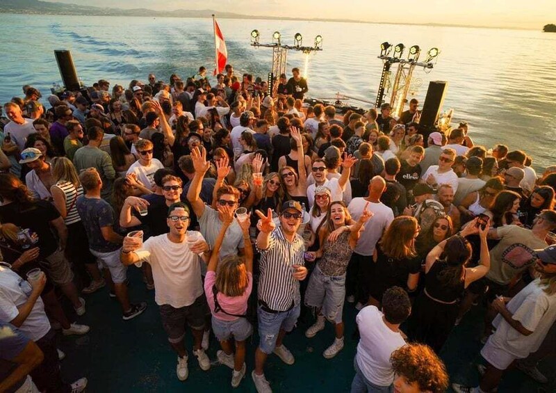 A crowd gathered on a boat by the water during sunset. 1