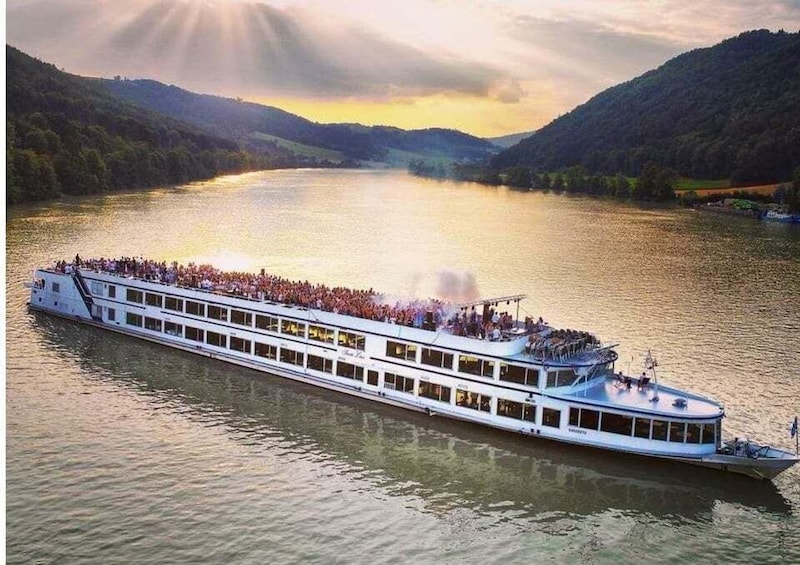 A riverboat with passengers, surrounded by hills and a sunset. 3