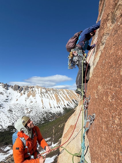 Two climbers ascending a rocky mountain with snow patches, under a clear blue sky. 4