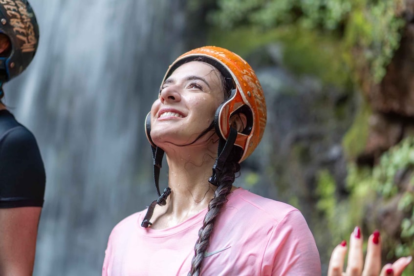 A person wearing a helmet and a pink shirt, standing near a waterfall. 1
