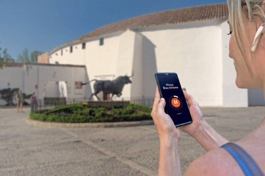 A person holding a smartphone with a music app interface, a bull statue, and a white building in the background. 5