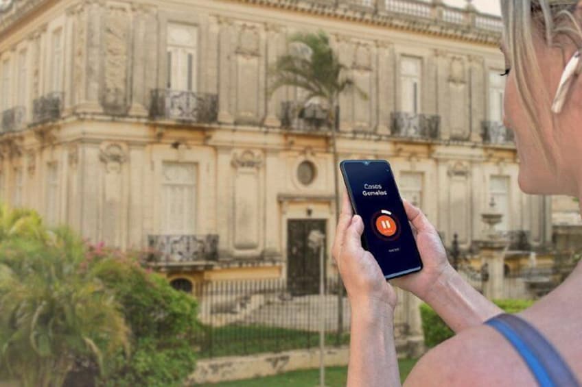 A person holding a smartphone with a music app open, standing in front of a historic building with ornate architecture. 5