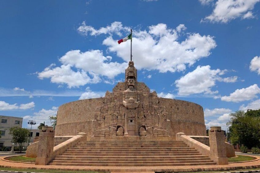 A large circular stone structure with a flagpole, steps leading up to it, and a clear blue sky. 3