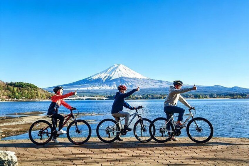 Three cyclists on a paved path by a lake with a mountain in the background. 1