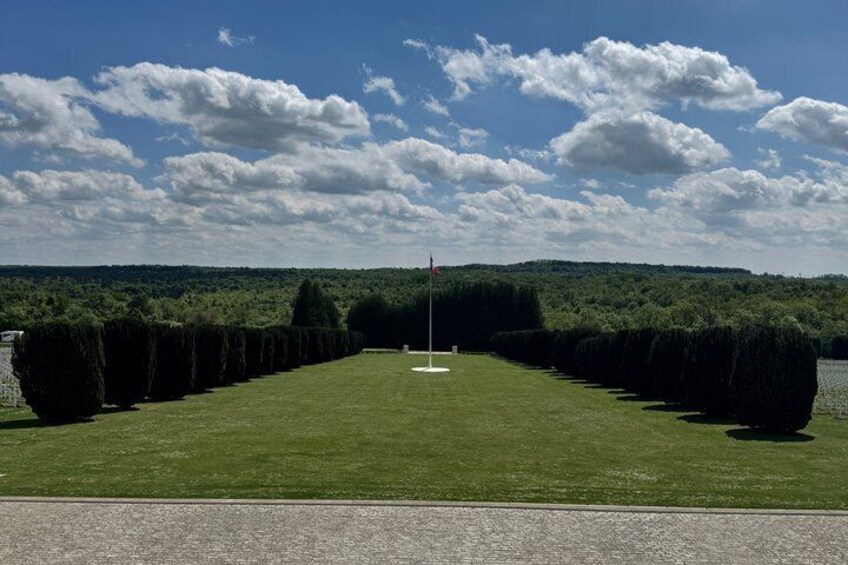 A well-manicured lawn with a flagpole in the center, bordered by neatly trimmed hedges, under a partly cloudy sky. 4
