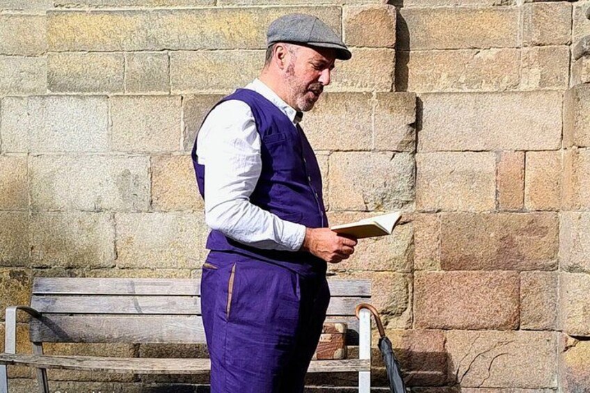 A person standing outdoors, reading a book, with a stone wall and a wooden bench in the background. 4