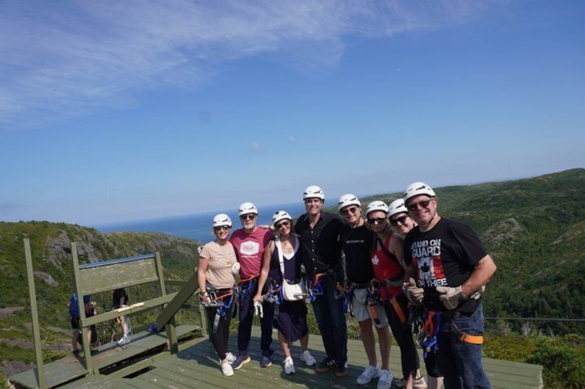 A group of people on a wooden platform with a scenic view of hills and ocean in the background. 4
