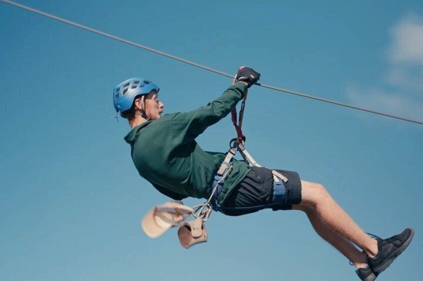 A person ziplining, wearing a helmet and harness, with a clear blue sky in the background. 1