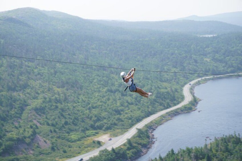 A person bungee jumping over a forested area with a river and road below. 2