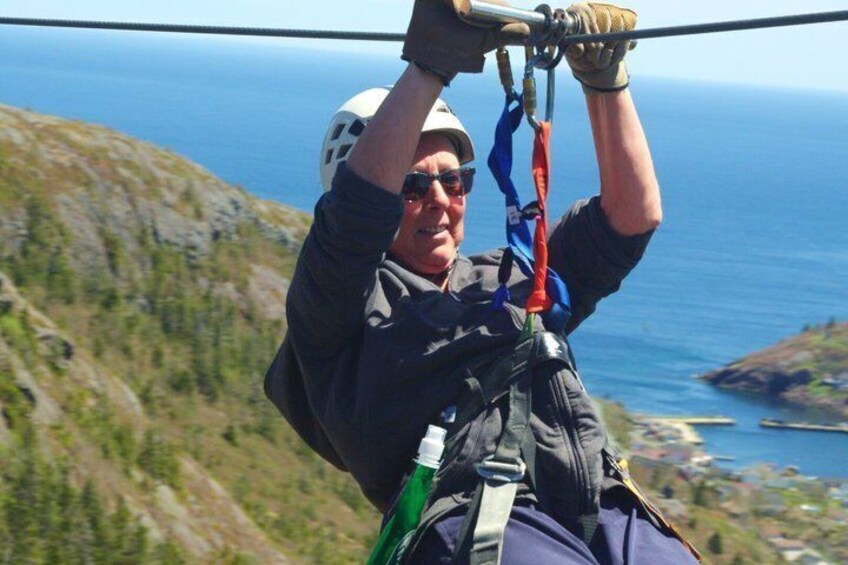 A person zip-lining with a helmet and harness, overlooking a coastal landscape. 5