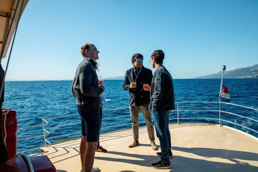Three people on a boat with a flag, ocean, and distant land. 1