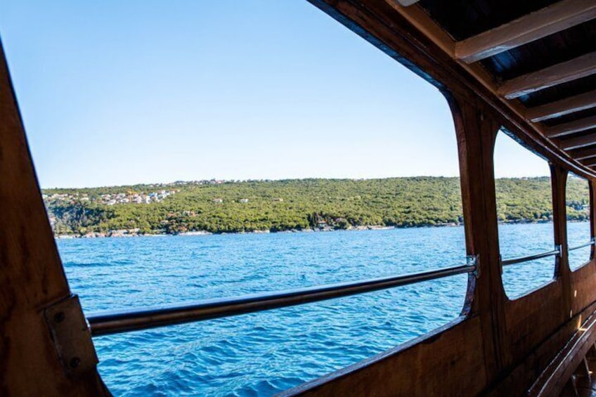 A wooden boat on a calm sea with a clear view of a coastline and buildings. 1