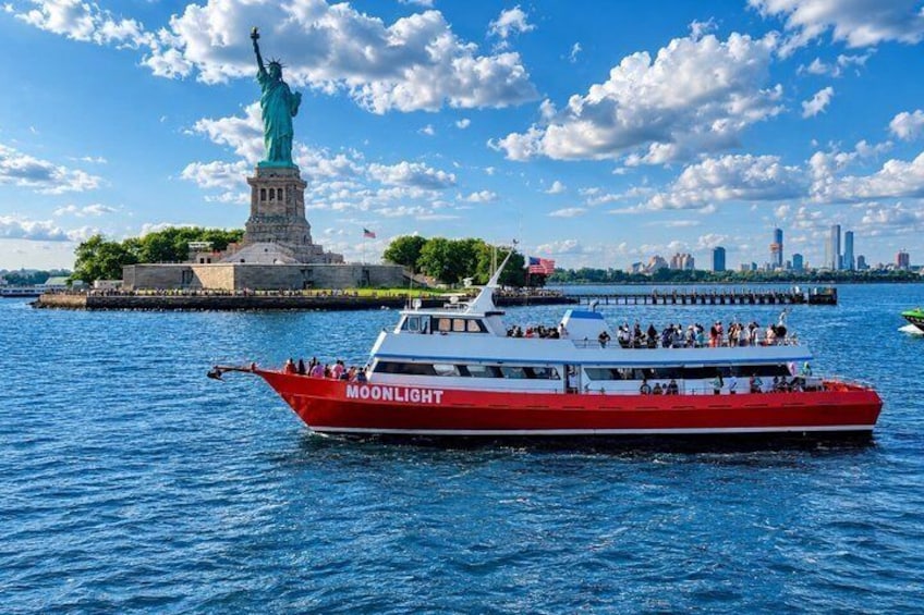 A red and white boat named 'MOONLIGHT' on the water with the Statue of Liberty in the background. 1
