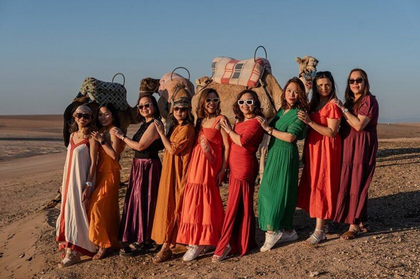 A group of people standing in a desert with camels in the background. 1
