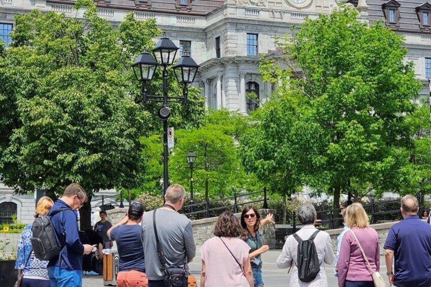 A group of people standing and walking in front of a historic building with trees and street lamps. 3