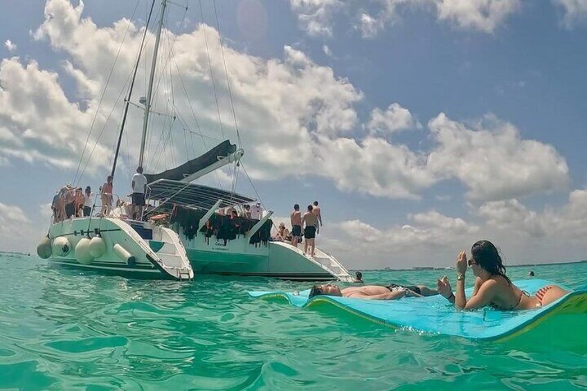 A sailboat with people on deck and a person lying on a floating mat in the water. 5