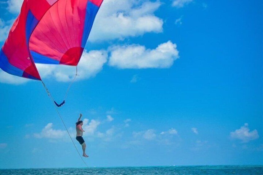 A person skydiving with a parachute over the ocean. 3