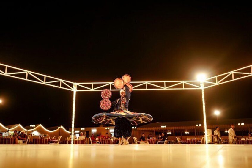 A nighttime outdoor event with a person performing on a skateboard, a crowd of spectators, and a brightly lit stage area. 2