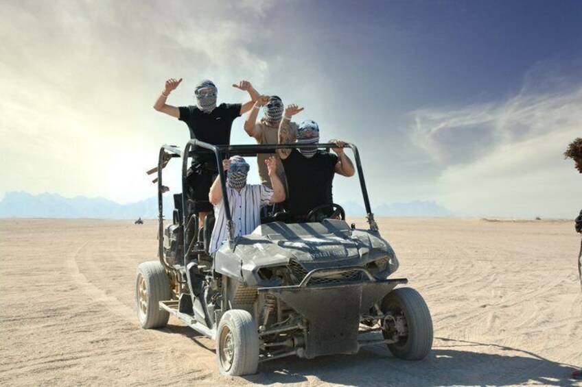 A group of people on a dune buggy in a desert landscape with mountains in the background. 1