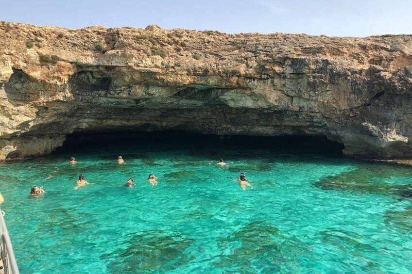 A group of people swimming in a clear blue sea under a rocky cave. 2