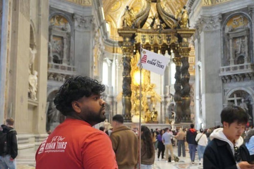 A person in a red shirt with 'Roman Tours' on the back, standing in a crowded, ornate interior with gold decorations and columns. 1