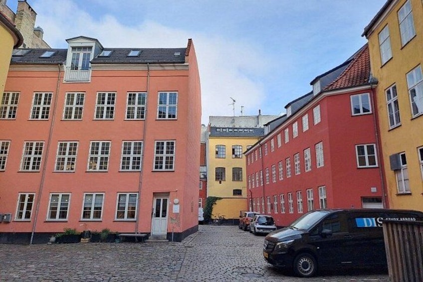 A cobblestone street lined with colorful buildings, a parked car, and a clear sky. 2