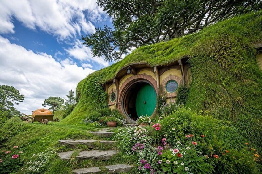 A Hobbiton-style house with a green door, surrounded by lush greenery and stone steps. 1