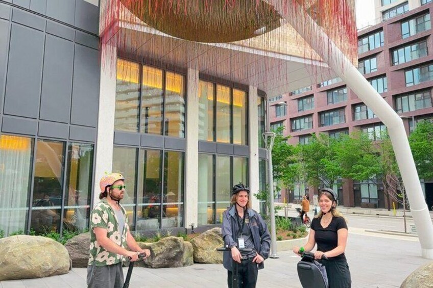 Three people standing in front of a modern building with large windows and a unique architectural feature. 3