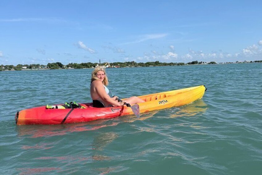 A person sitting on a yellow kayak in calm water with a distant shoreline. 3