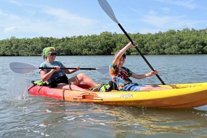 Two people kayaking on a calm river with dense greenery in the background. 5