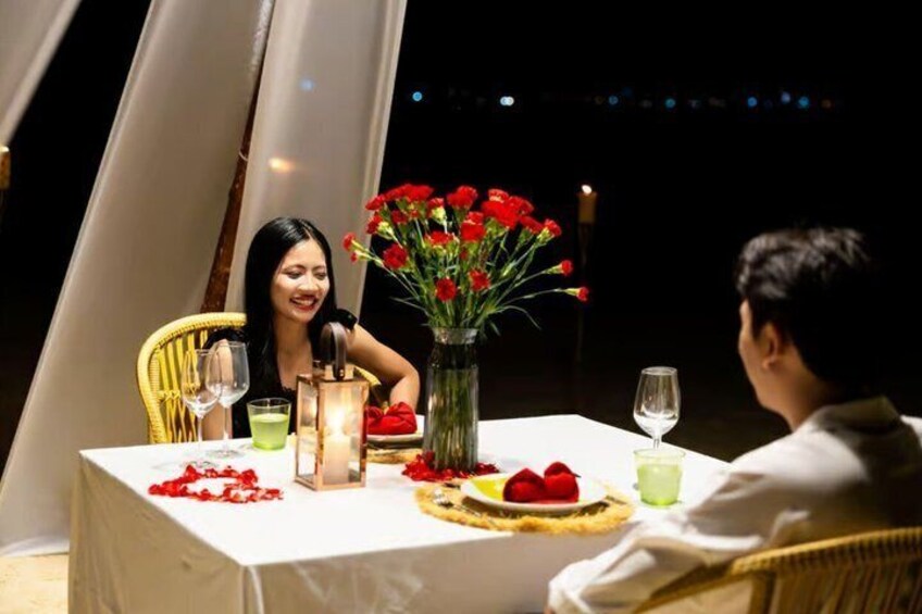 A couple dining at a table with a candle, flowers, and a fruit plate. 4