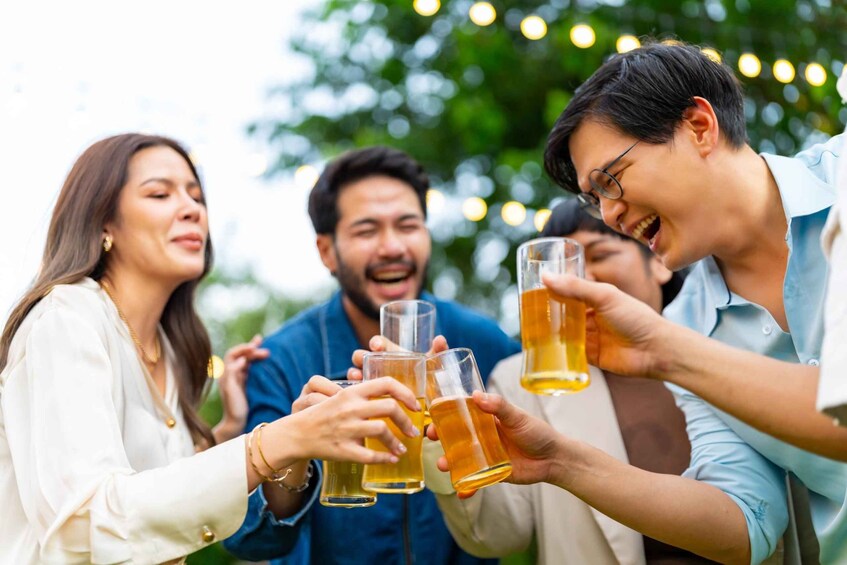A group of people toasting with beer glasses outdoors, surrounded by greenery and string lights. 3