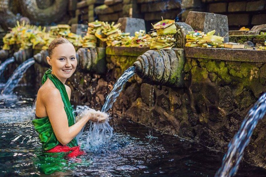 A person in a green garment standing in water with multiple water spouts. 4