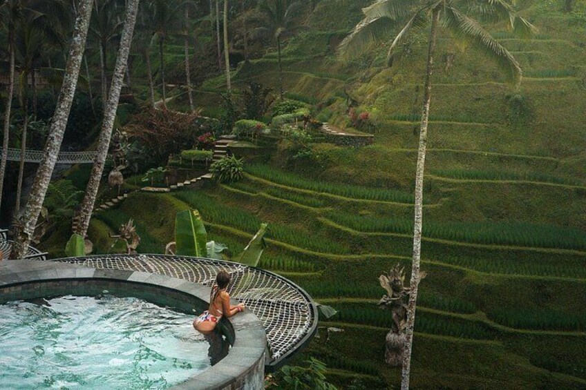 A person in a bikini sitting on a hot tub surrounded by lush green terraced fields and palm trees. 4