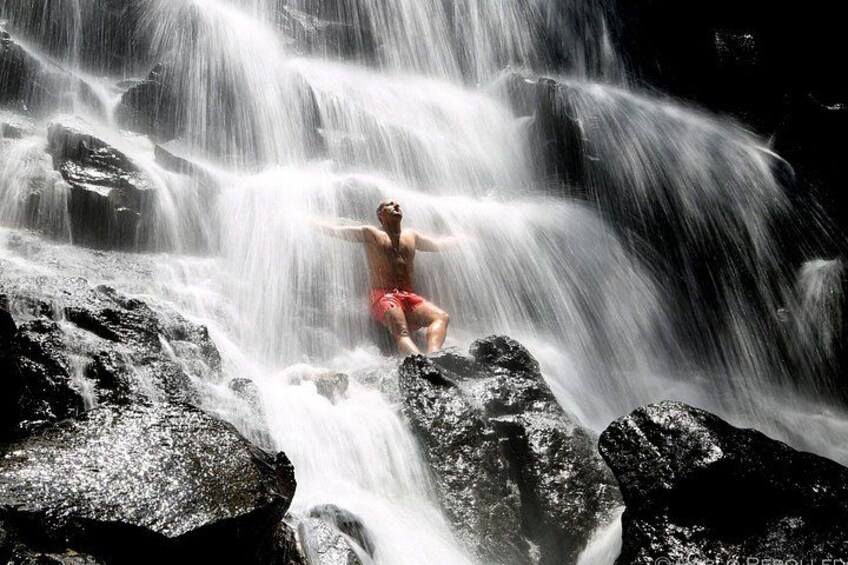 A person standing on rocks with arms outstretched in front of a waterfall. 2