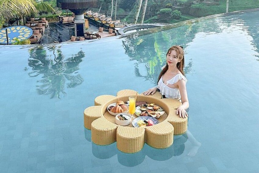 A person sitting on a floating wicker table with food and drinks by a pool. 5