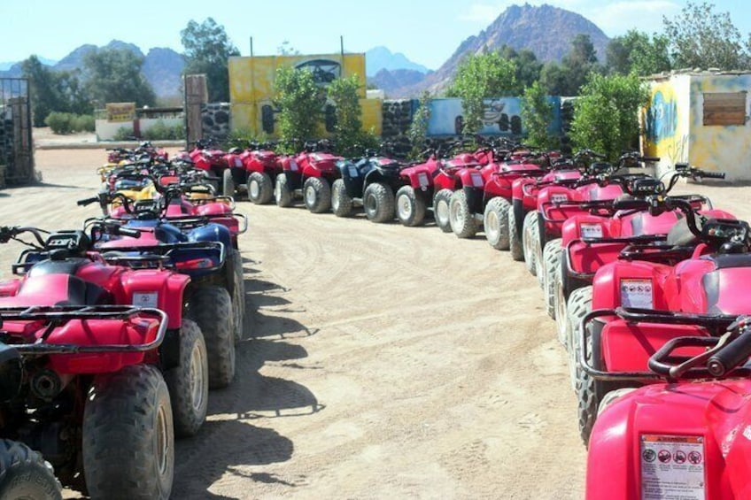 A row of red quad bikes parked on a dirt road with mountains in the background. 4