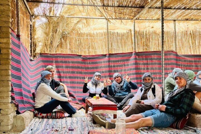 A group of people sitting in a circle under a thatched roof, engaged in a discussion. 2