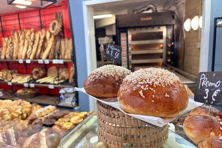 Una vetrina di panetteria con pane e dolci, un cartello che indica una promozione e un forno a legna sullo sfondo. 3