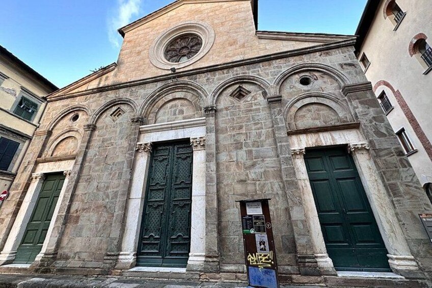 A historic stone building with arched windows and doors, and a circular window above the central door. 3