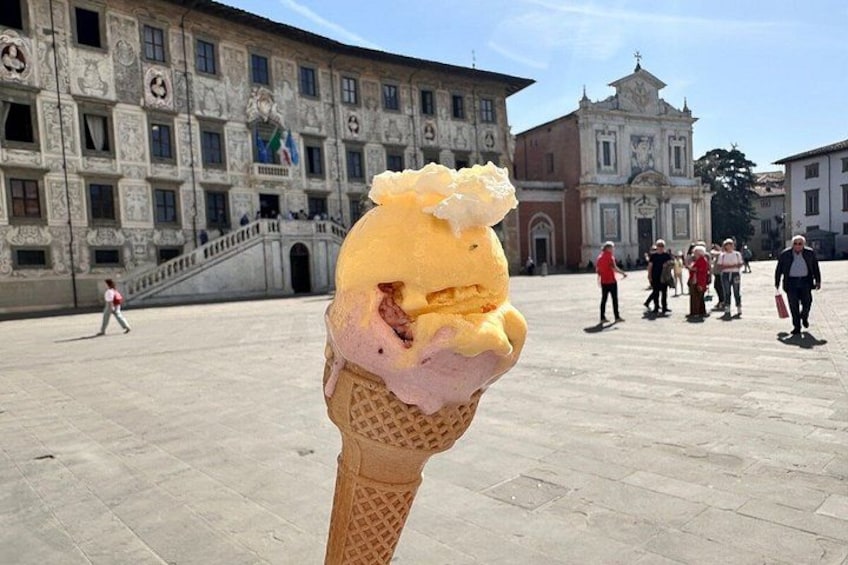 An ice cream cone in front of a historic building with people walking in the background. 5
