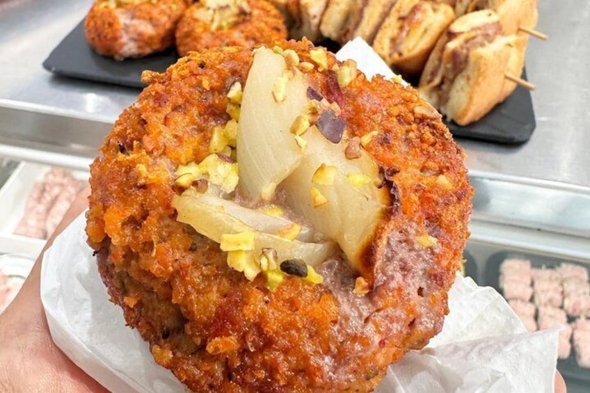 A hand holding a fried pastry with a crispy, golden-brown exterior and a visible filling of onions and nuts. 5